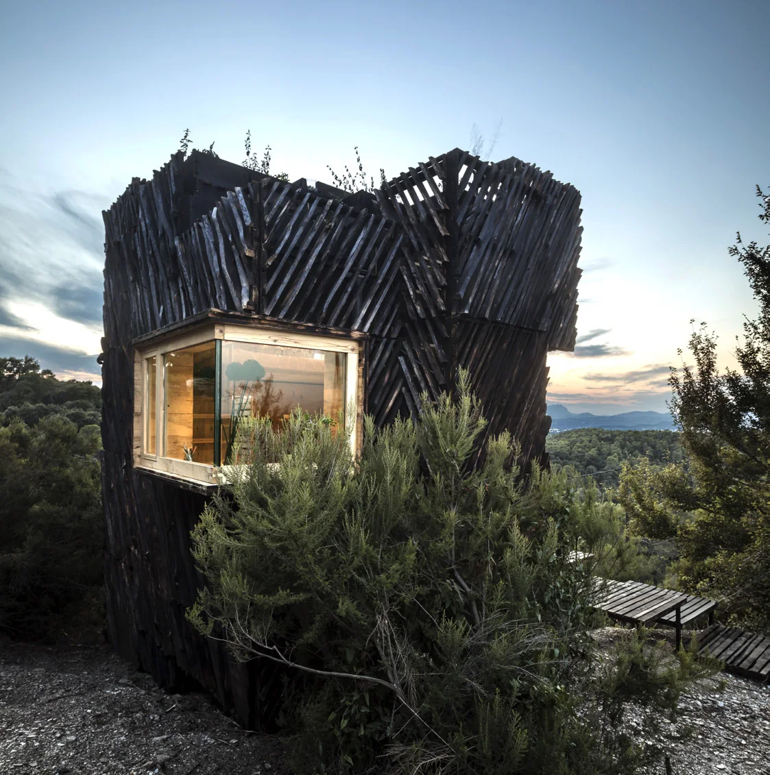 The Voxel timber cabin at dusk with a lit window among dark trees