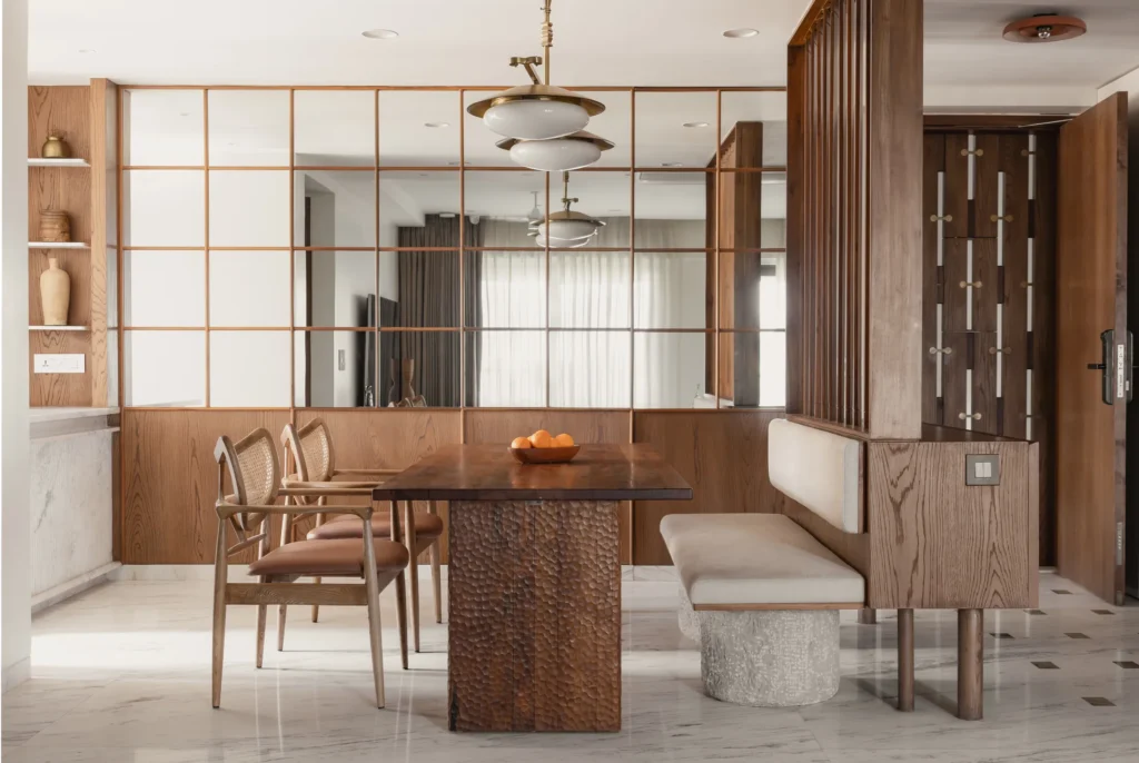Dining area with a carved timber table, stone-legged bench and a mirrored wall reflecting daylight in home in•between