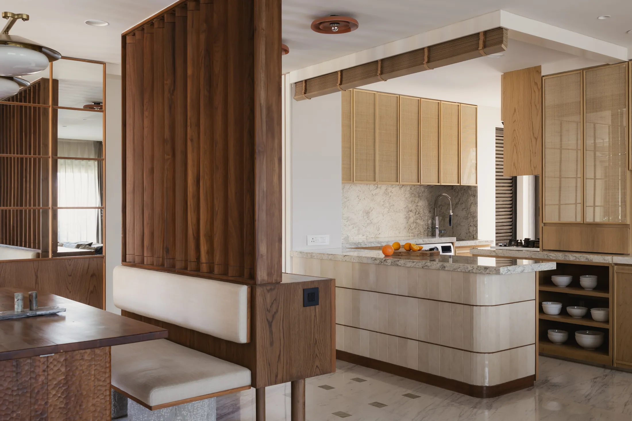 home in•between kitchen with a curved pale stone island and upper cabinets, seen past a timber screen