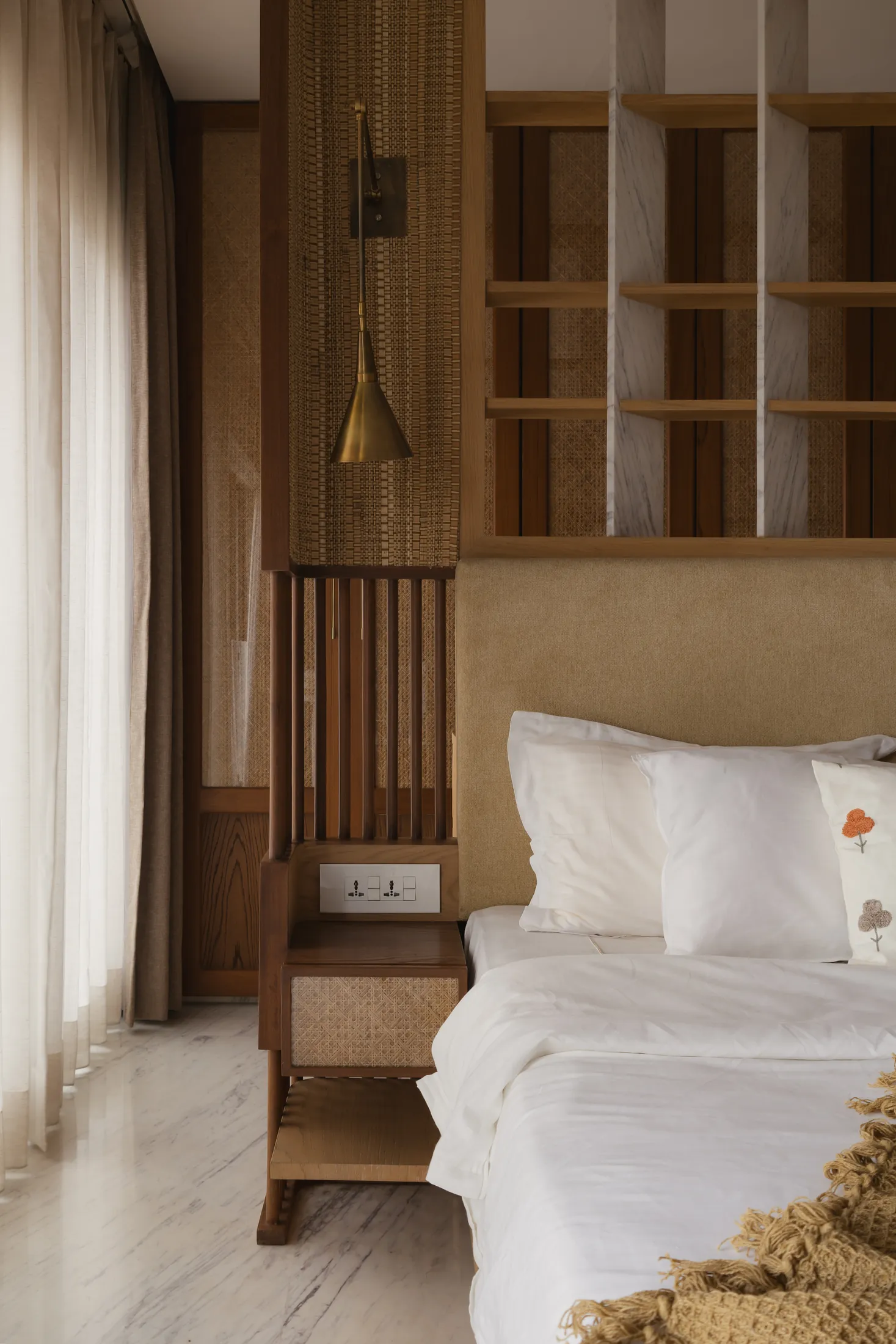 home in•between bedside with built-in timber shelving headboard, cane side table and brass lamp