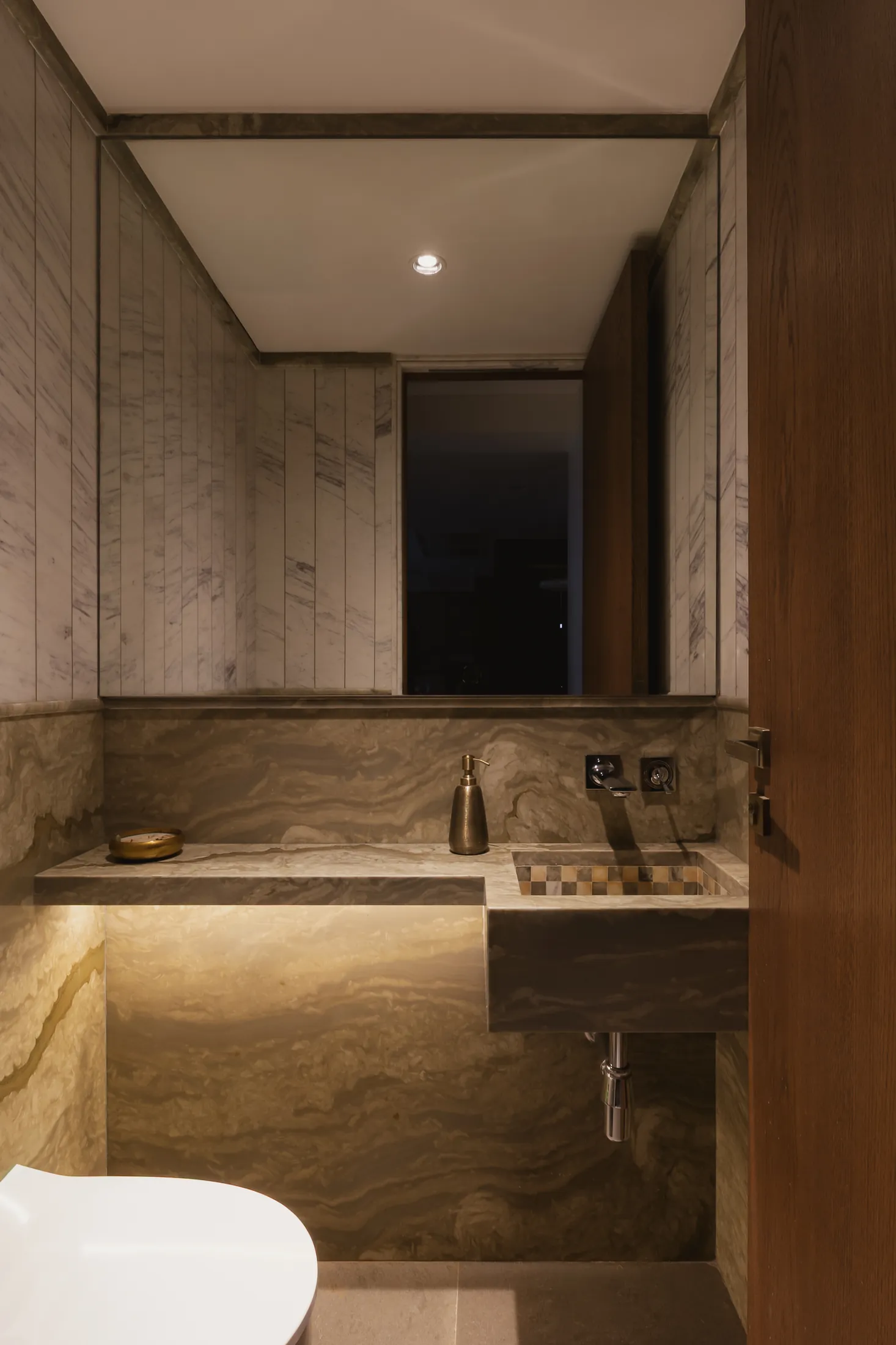 home in•between powder room with veined stone walls and a backlit stone basin counter