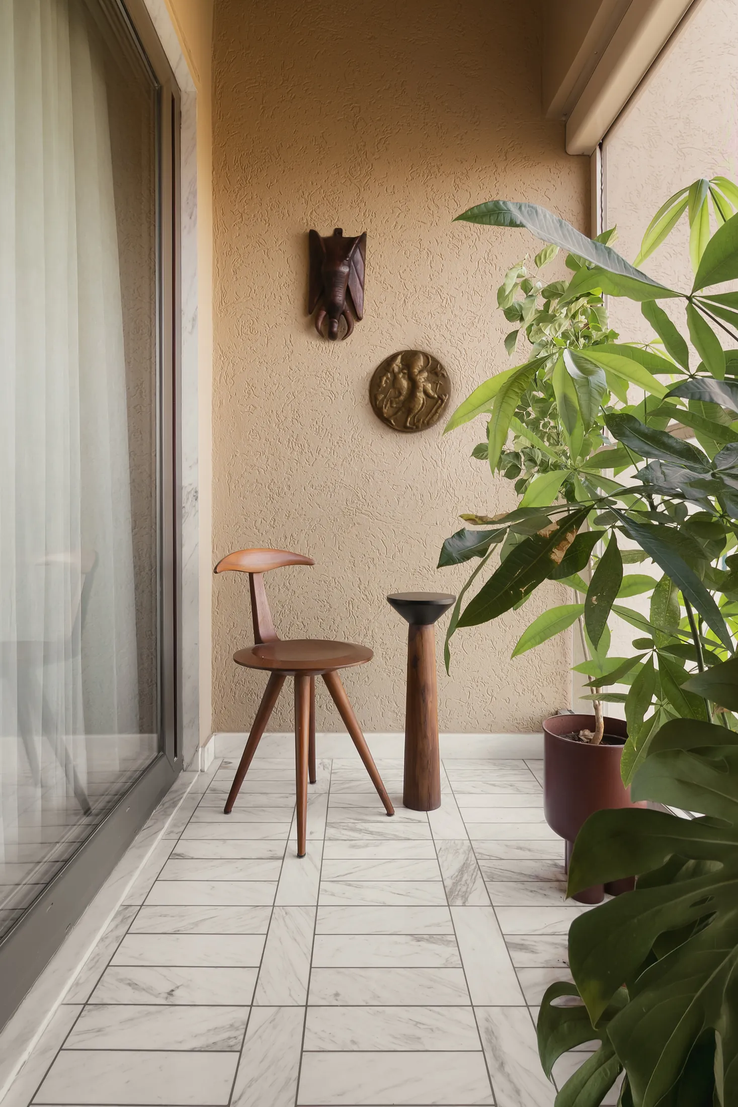 home in•between balcony corner with a timber stool, potted plant and terracotta wall piece