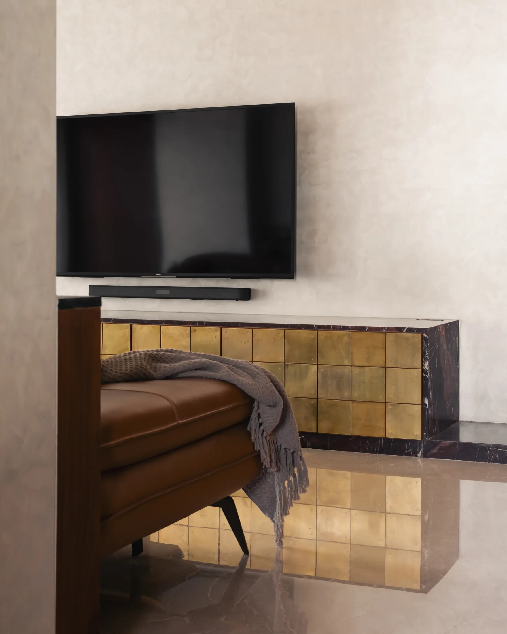Plum House brass-tiled TV console on a red marble base, reflected in the polished floor
