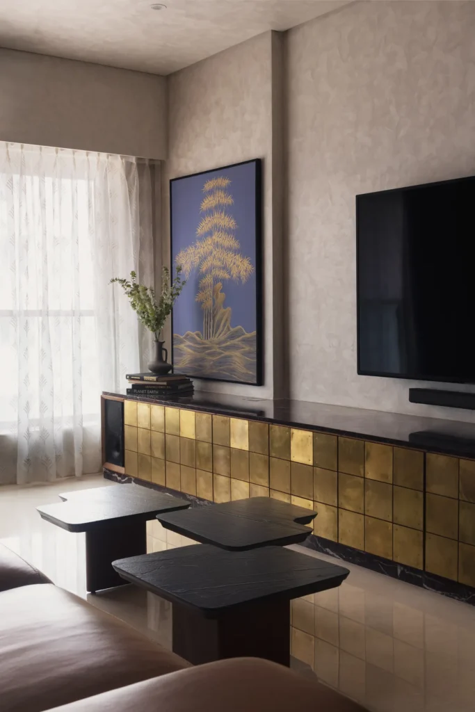 Plum House living room with a raw brass TV console, nesting black marble coffee tables and a botanical artwork