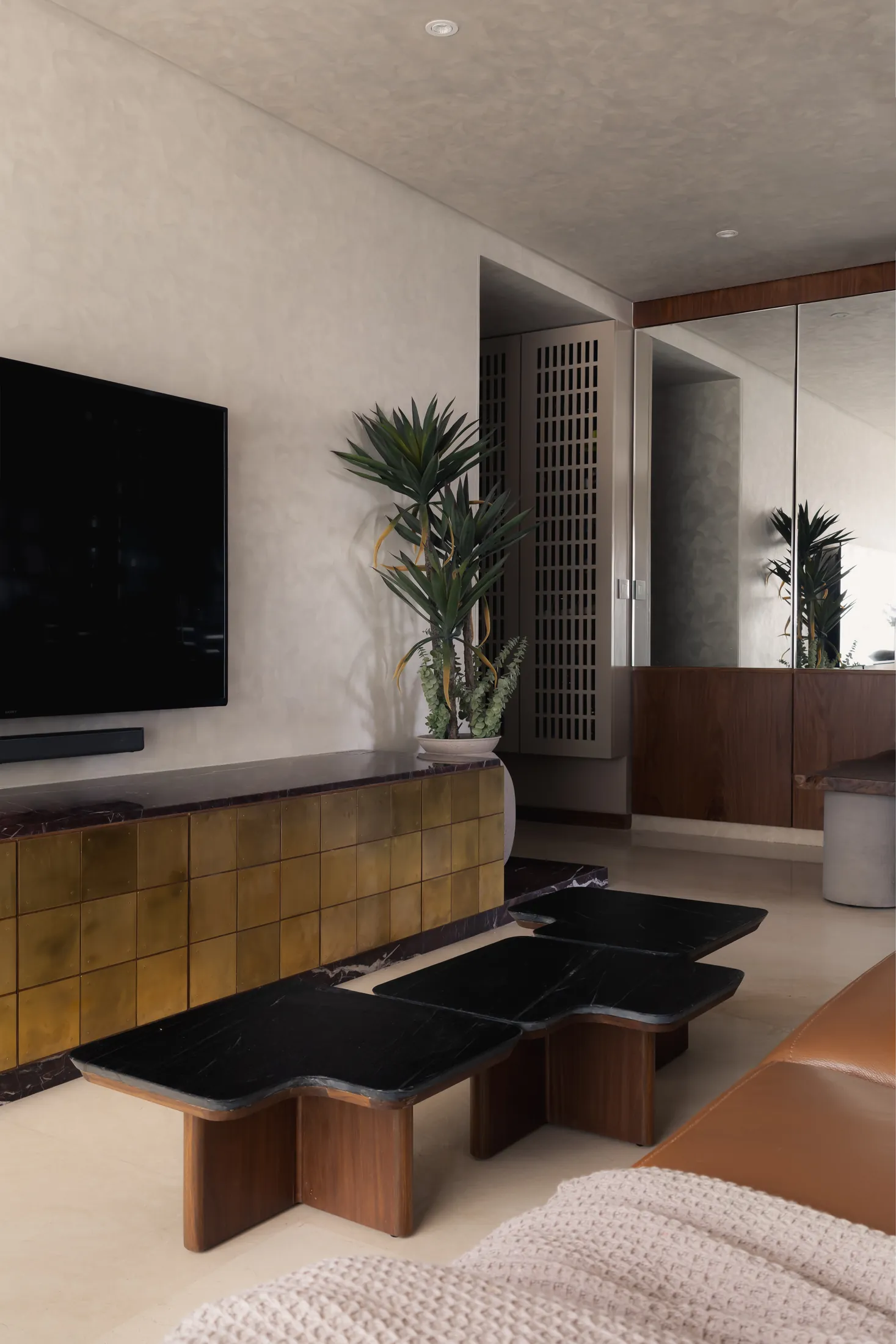 Plum House living room with a brass-tiled TV console, black marble coffee tables and mirrored storage wall