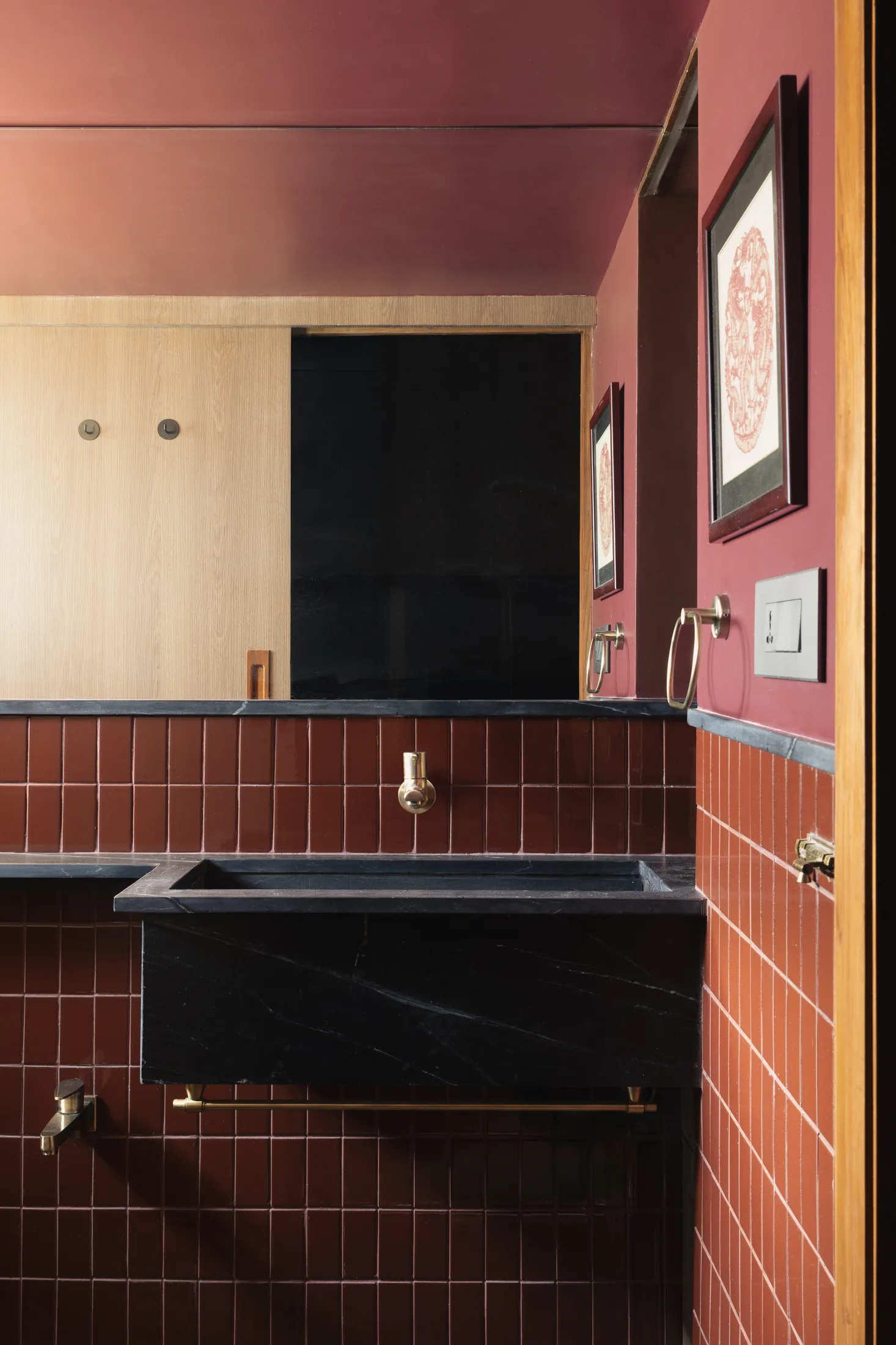 Plum House bathroom with terracotta-red tiles, a black stone basin and a brass tap