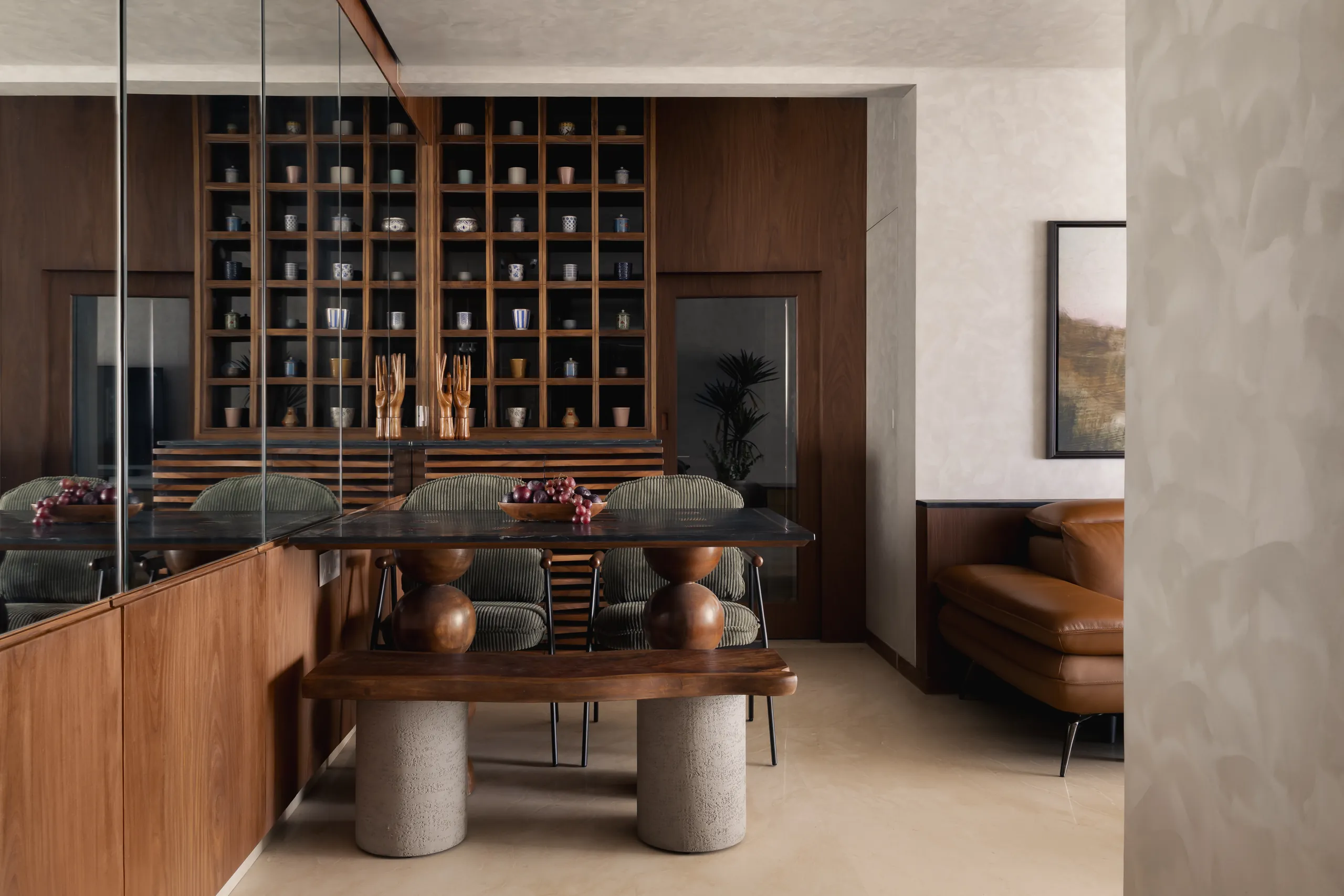 Plum House dining area with a black marble table on stone columns and a lit teak display wall