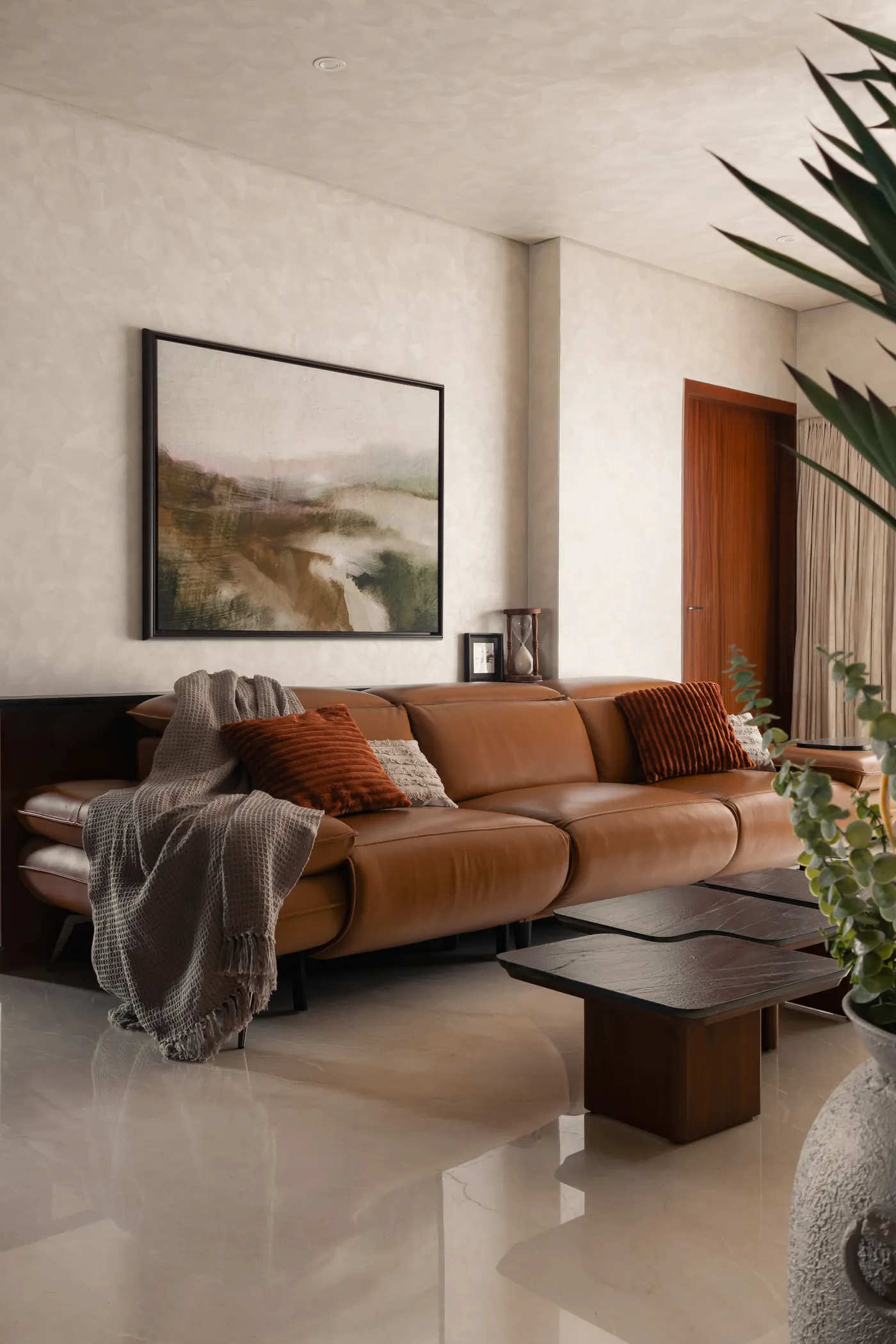 Plum House living room in Breach Candy, Mumbai, with a tan leather sofa, textured plaster walls and a low timber coffee table