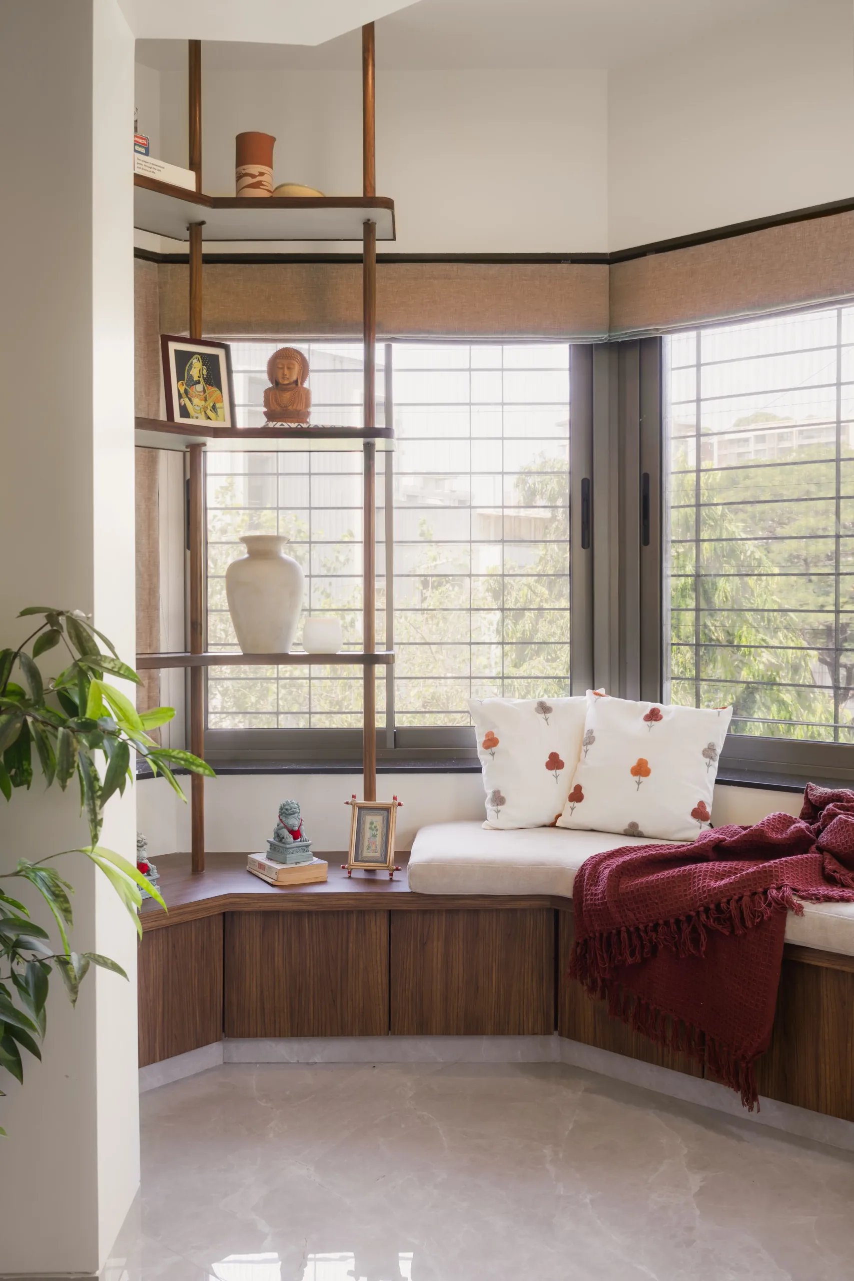 The Nest corner window seat with open timber display shelves and a burgundy throw