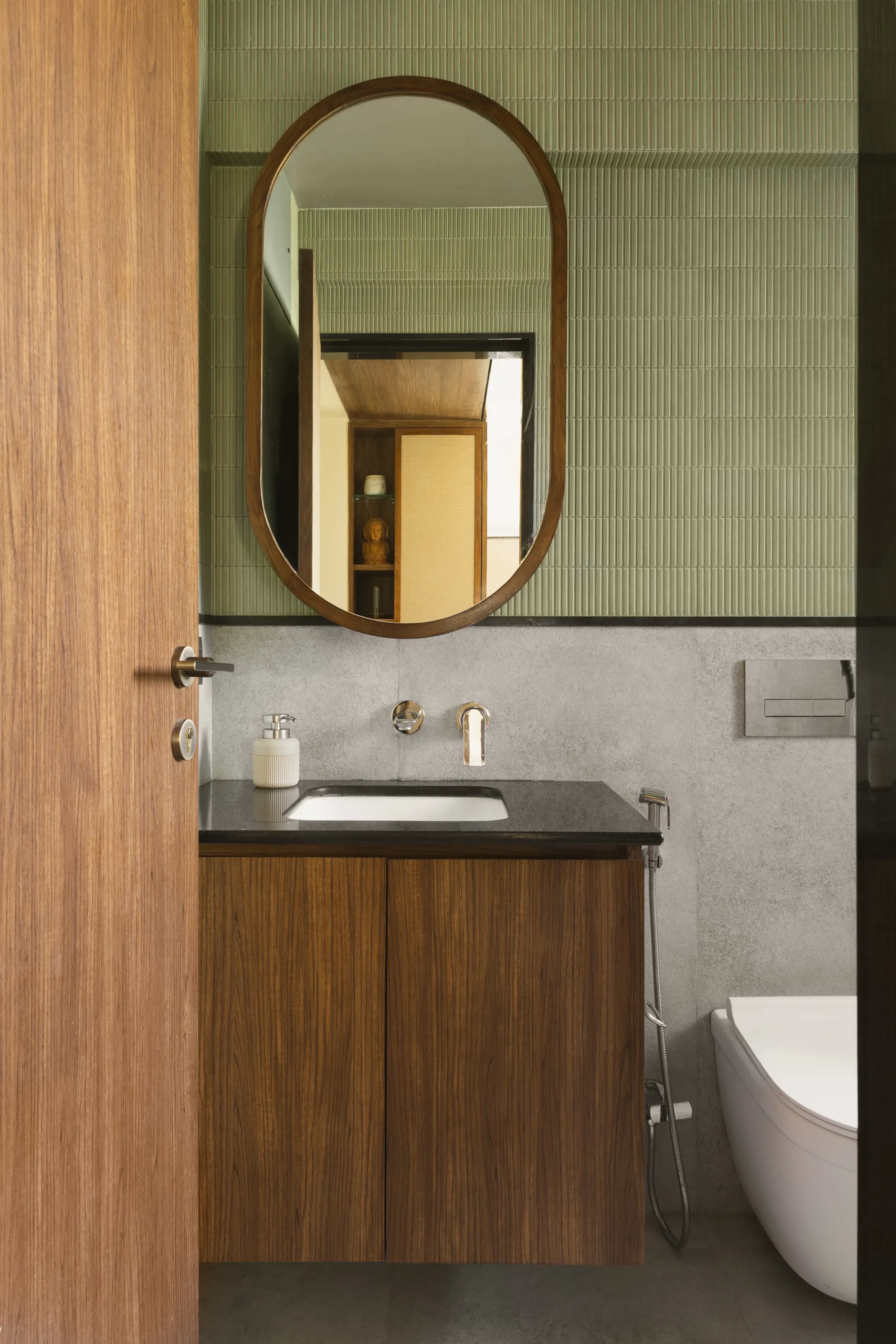 The Nest bathroom with an oval mirror, green fluted tiles and a timber vanity with a black counter