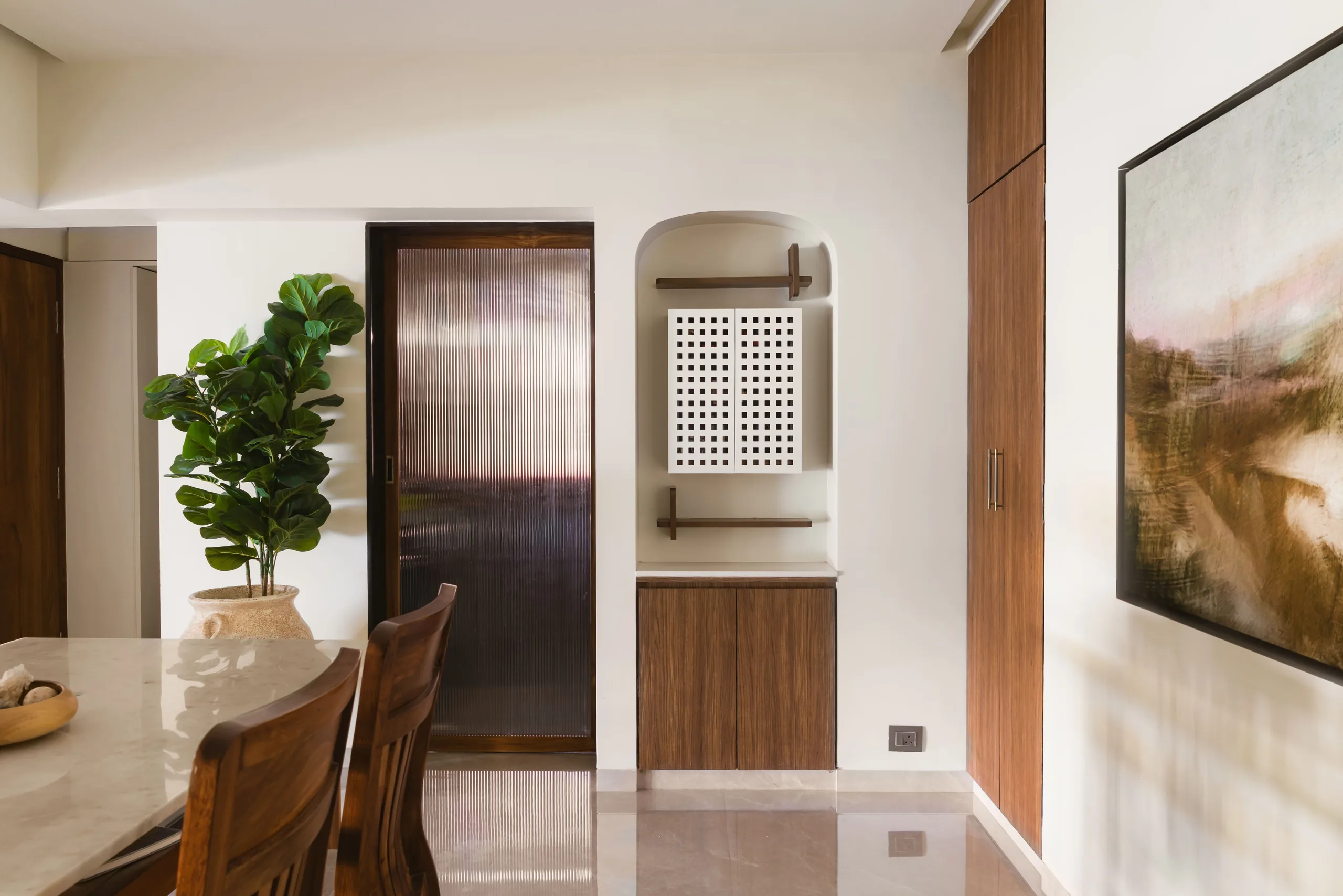 The Nest dining corner in Juhu with a timber dining set, arched niche, wooden door and landscape painting