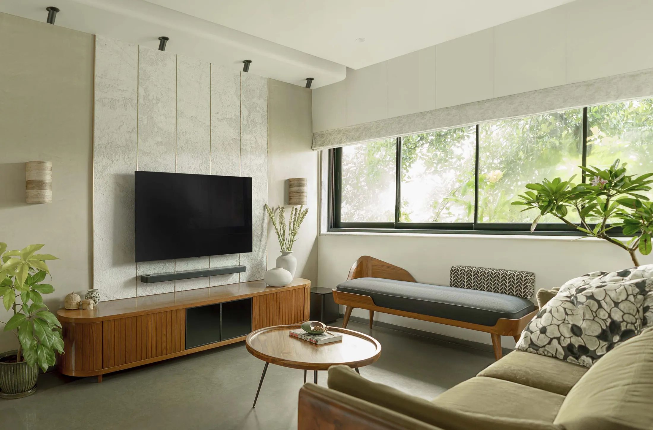 The Seed living room with a lime-plaster TV wall, teak console, daybed and a window onto trees