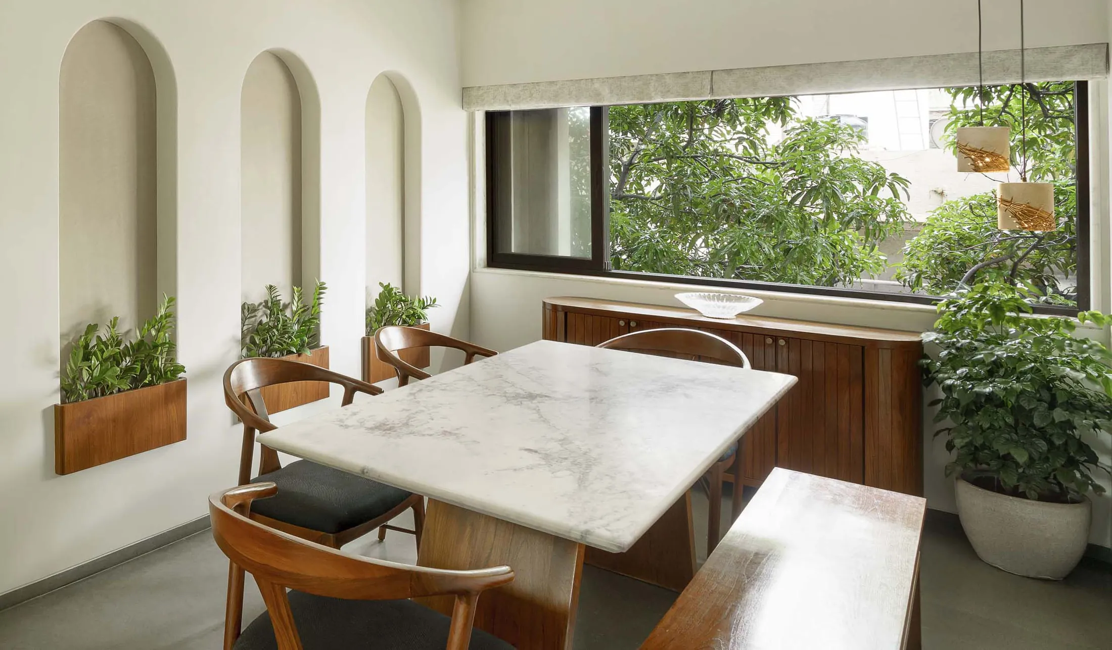 The Seed dining area with a white marble table, arched plaster niches with plants and a window to trees