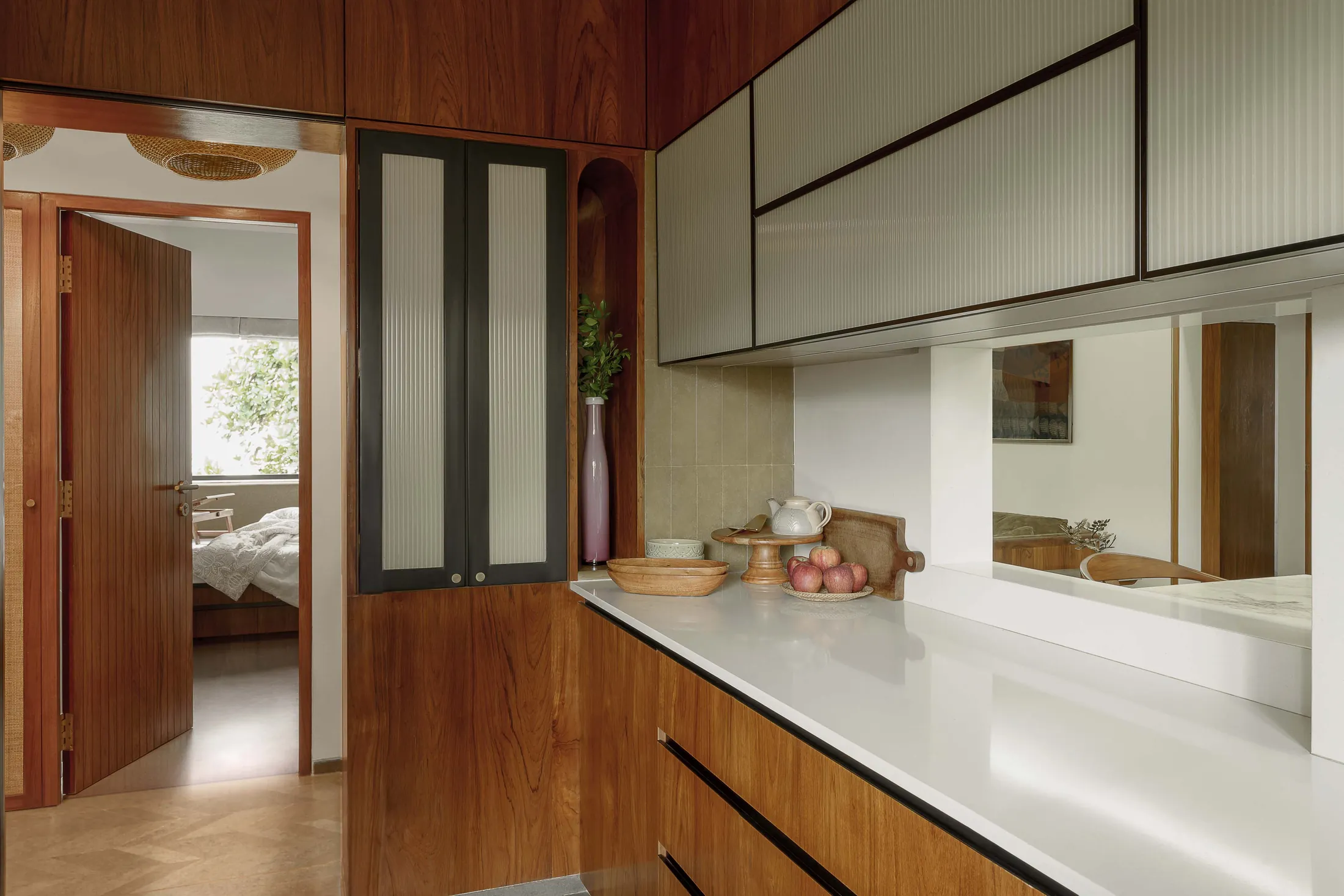 The Seed kitchen with a white counter, teak cabinets and fluted glass, with a view into the passage