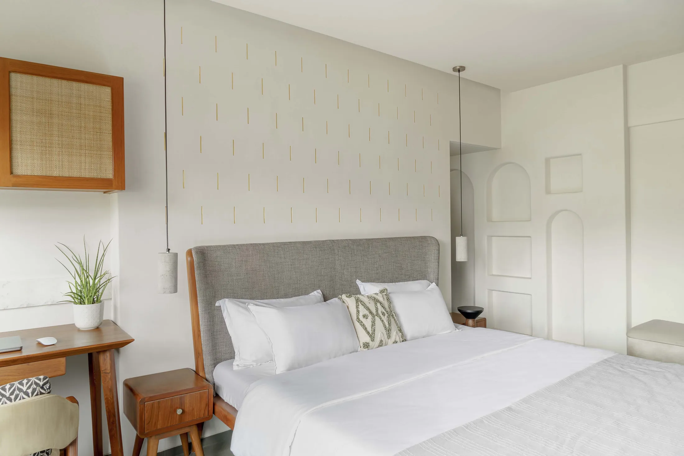The Seed bedroom with a grey upholstered bed, cane wall frame, plaster niches and a desk by the window