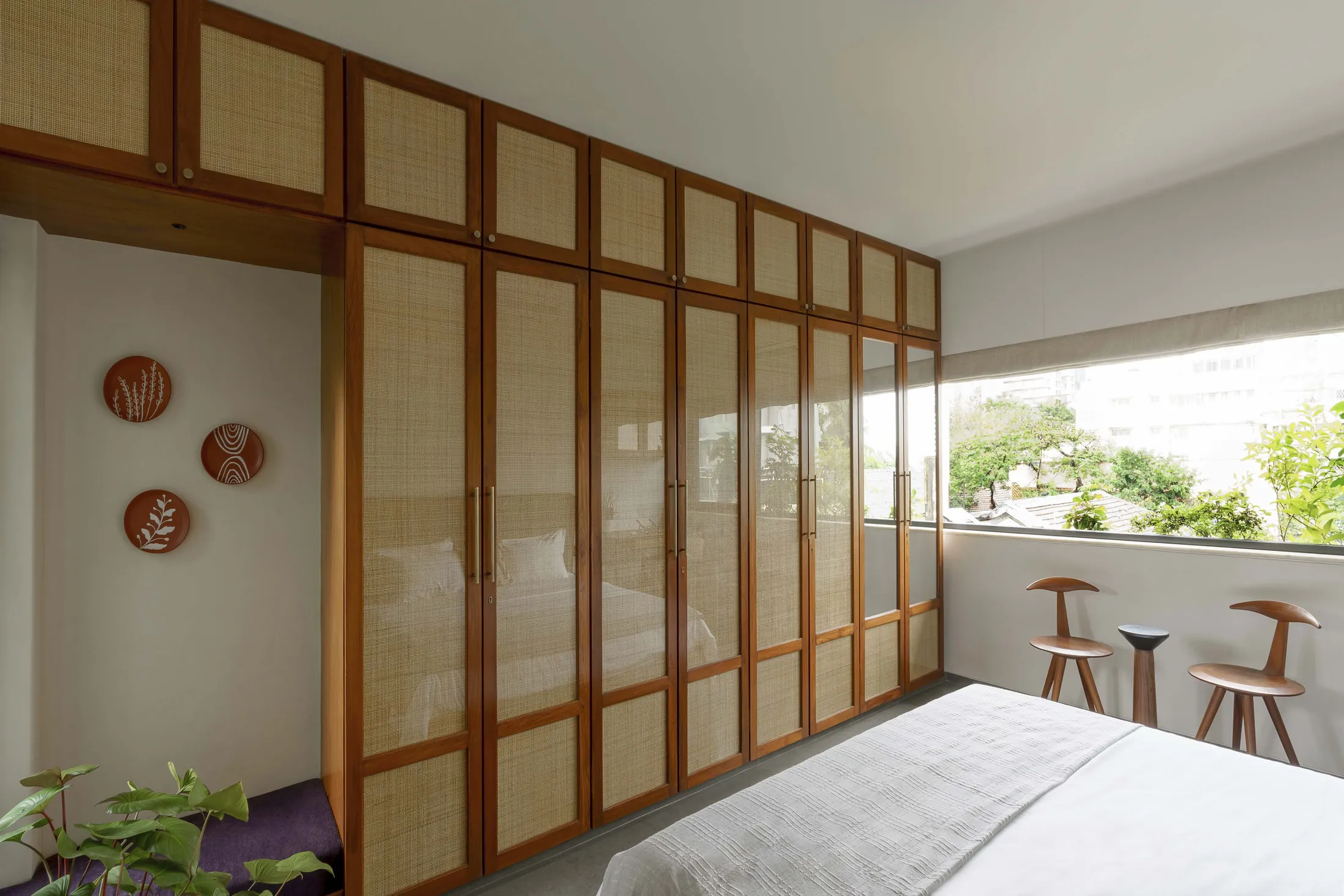 The Seed bedroom with teak-framed rattan wardrobe doors, terracotta wall plates and a balcony window