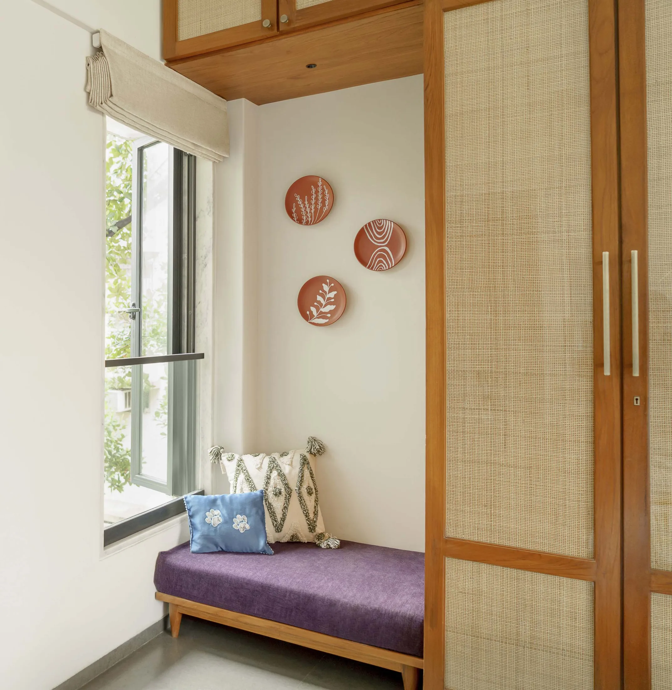 The Seed window seat with purple upholstery beside rattan-panelled wardrobes and terracotta plates