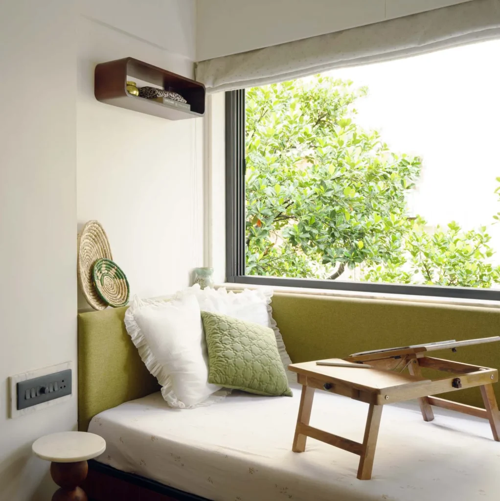 Daybed under a large window framing jackfruit leaves, with a folding teak tray table, in The Seed