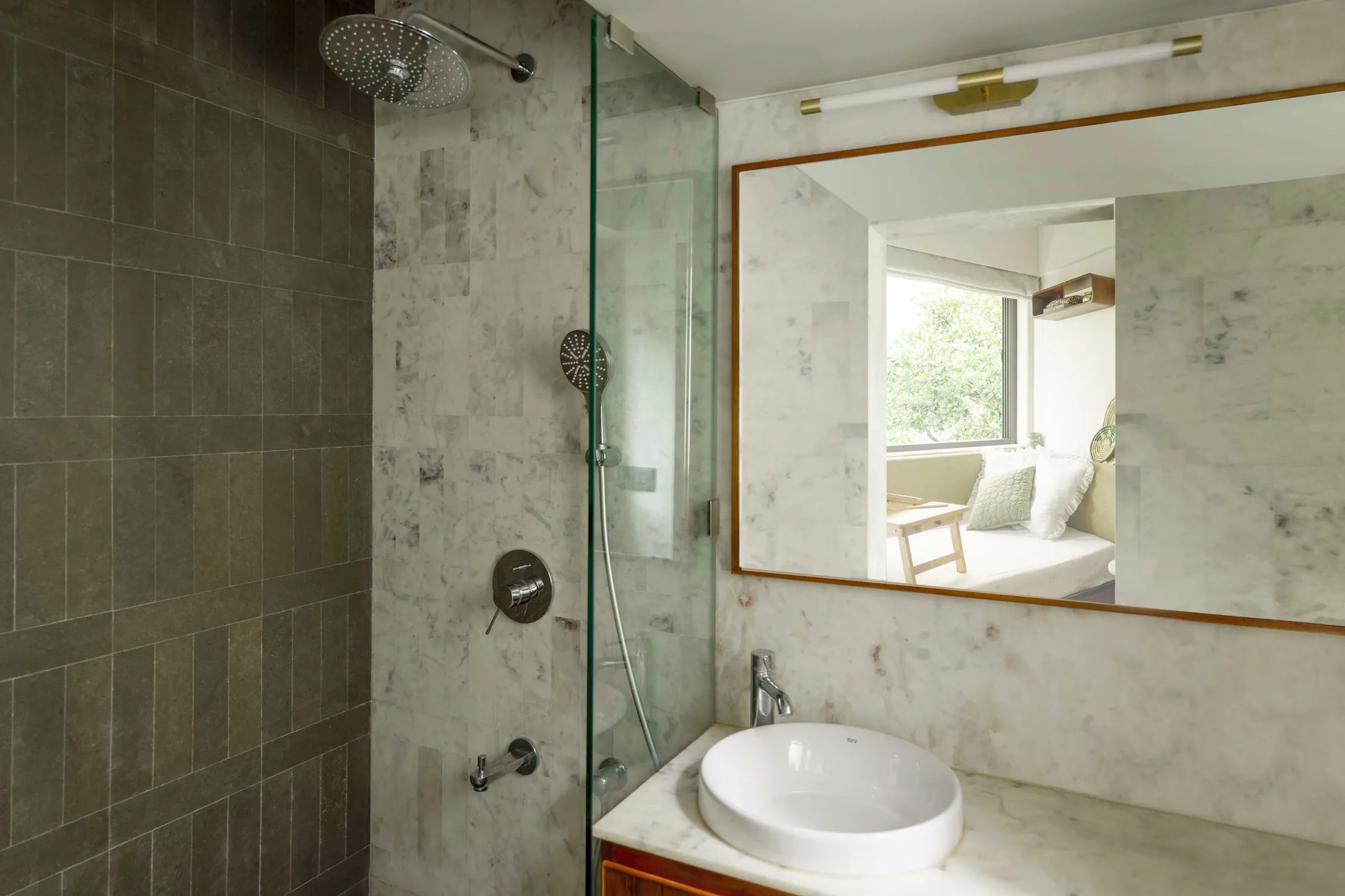The Seed bathroom with stone-look walls, a glass shower partition, round basin and teak-framed mirror