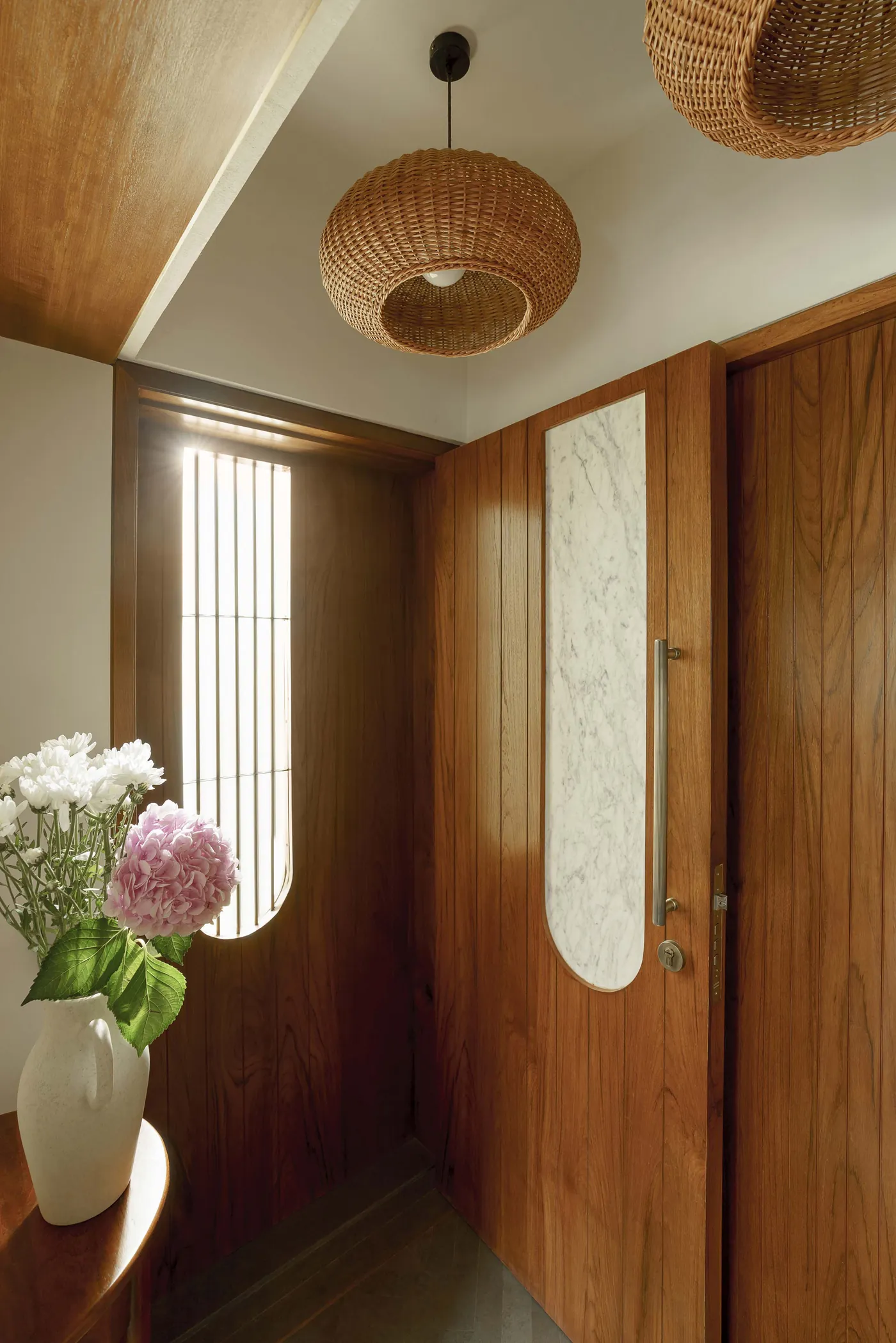 Entrance of The Seed with a teak door, rattan pendant lights and an arched marble inlay
